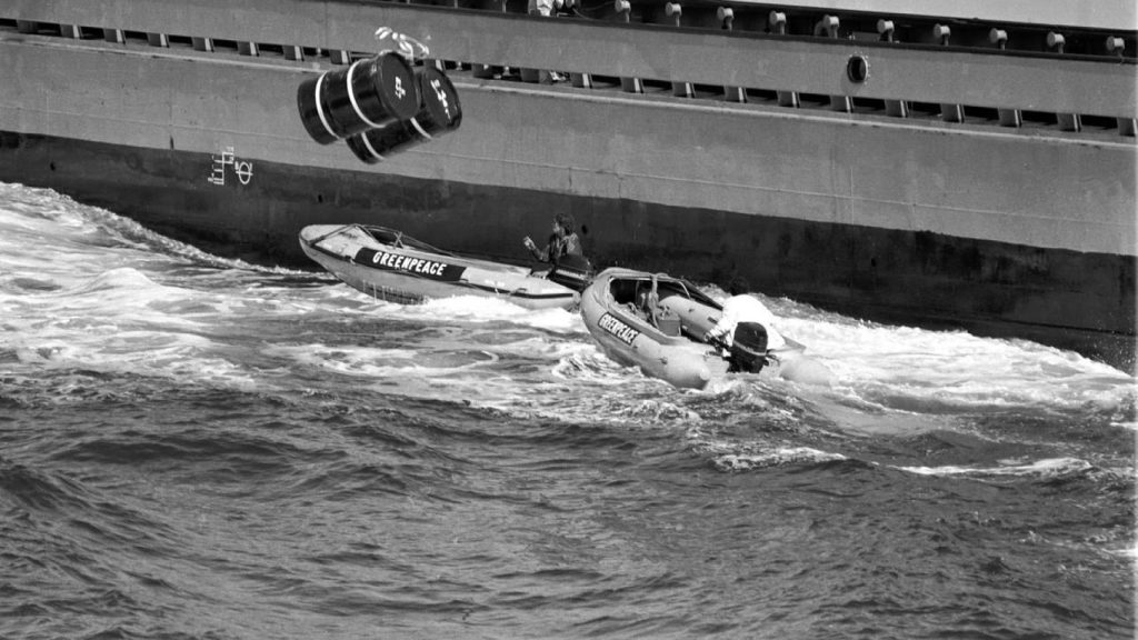 ativista ambiental arrisca a vida no mar interceptando barris a cair na água com lancha motora - 1980