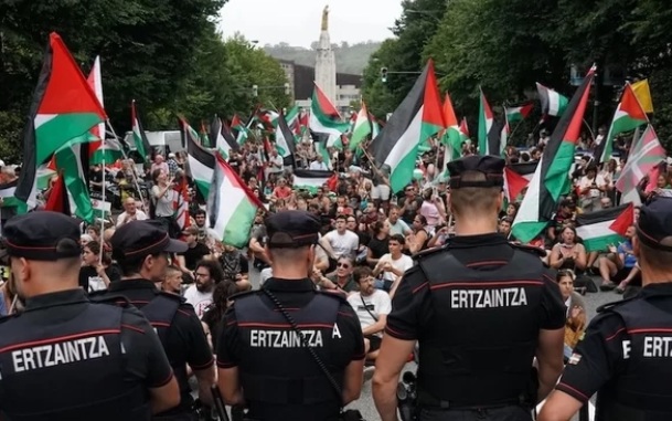 Imagem de centenares de pessoas sentadas com bandeiras palestinas a impedir o trânsito, vigiadas pela polícia basca