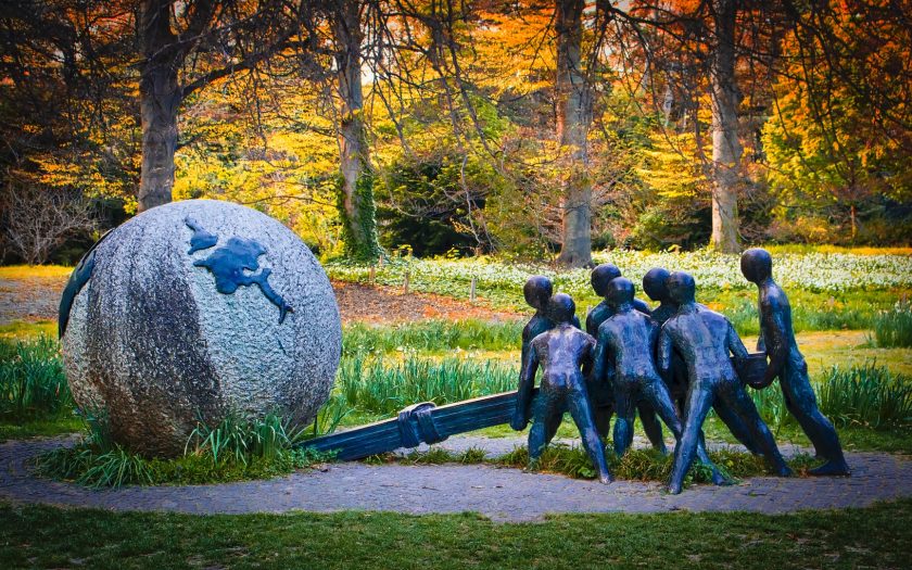 Escultura em metal de grupo humano a mover uma bola do mundo de pedra com uma alavanca