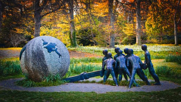 Escultura em metal de grupo humano a mover uma bola do mundo de pedra com uma alavanca