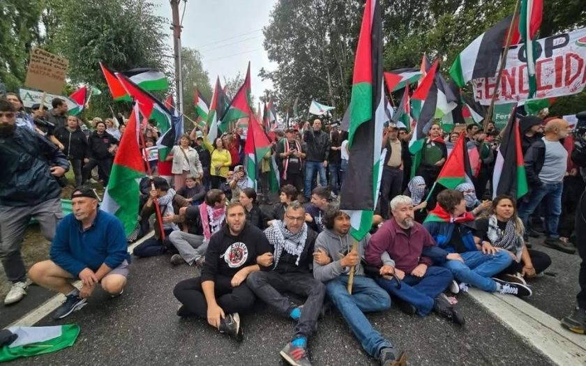 Pessoas sentadas na estrada a cortar o trânsito rodeadas de bandeiras palestinianas e faixas de protesto