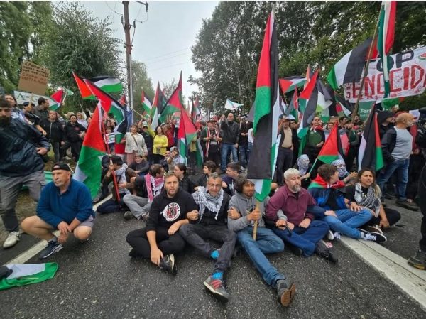Pessoas sentadas na estrada a cortar o trânsito rodeadas de bandeiras palestinianas e faixas de protesto