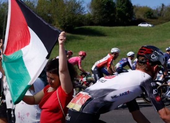 mulher segurando bandeira da palestina no meio da corrida ciclista