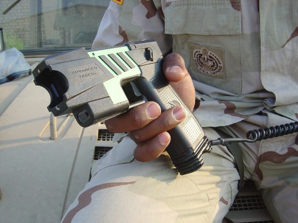 Polícia sentado segurando um Taser sobre o joelho, um arma de eletrochoque de uso interdito no espaço público em Portugal