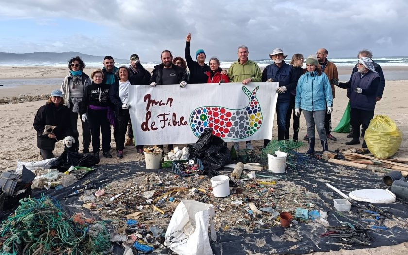 voluntários na praia atrás duma faixa da associação com lixo recolhido do mar à frente