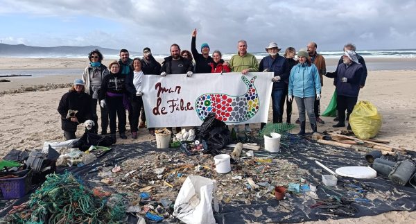 voluntários na praia atrás duma faixa da associação com lixo recolhido do mar à frente