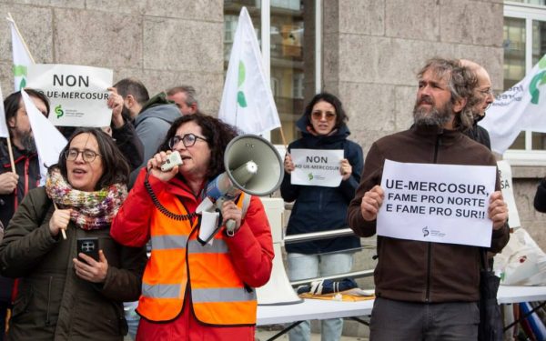 imagem do protesto com mulher com megafone e um cartaz a dizer "Mercosur: fome pro norte e fome pro sul"