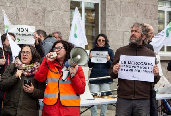 imagem do protesto com mulher com megafone e um cartaz a dizer "Mercosur: fome pro norte e fome pro sul"