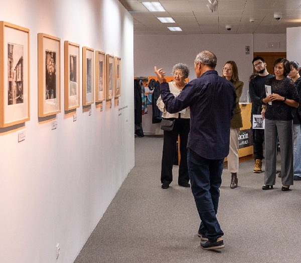 Fotografias do autor na parede e pessoas a olhar com alguém a explicar