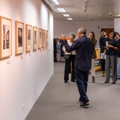 Fotografias do autor na parede e pessoas a olhar com alguém a explicar